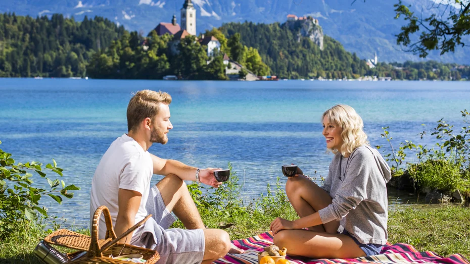 Mlajši par sproščeno uživa na pikniku ob Blejskem jezeru