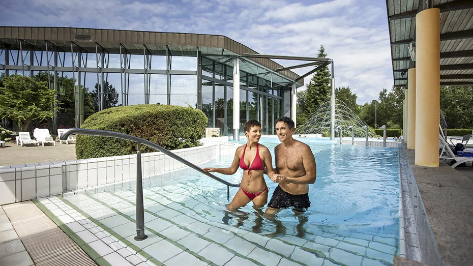 Moški in ženska v kopalkah izstopata iz zunanjega bazena in se držita za roke