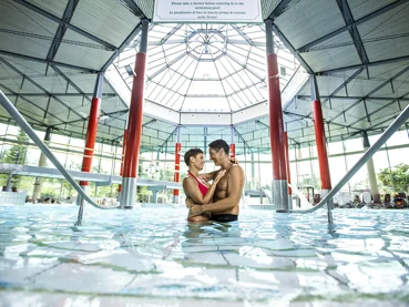 Par se zaljubljeno gleda in objema na sredini notranjega bazena
