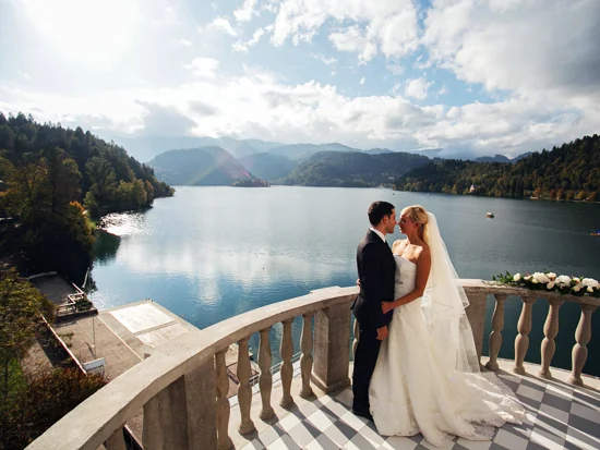 Ženin in nevesta na poročnem obredu stojita na terasi s pogledom na blejsko jezero
