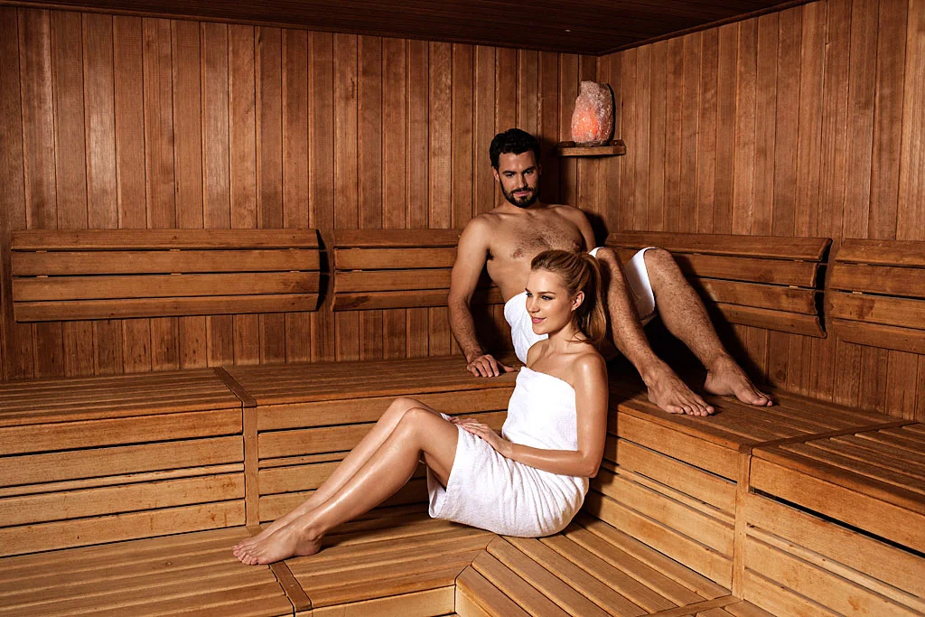 Moški in ženska v belih brisačah uživata in se sproščata v romantični leseni savni