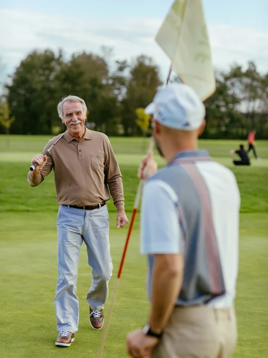 Dva športno oblečena moška z golf palicama se pogovarjata na golf igrišču