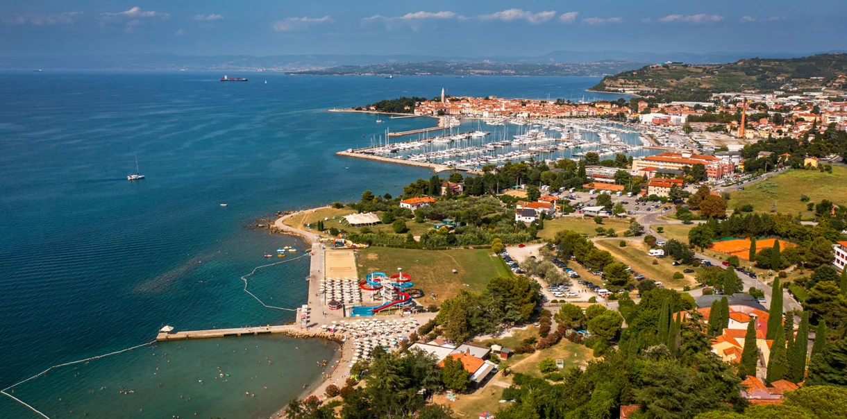 Panoramski pogled na slovensko obalo, ki vključuje pristanišče, hotelski kompleks, staro mestno jedro in zelene površine
