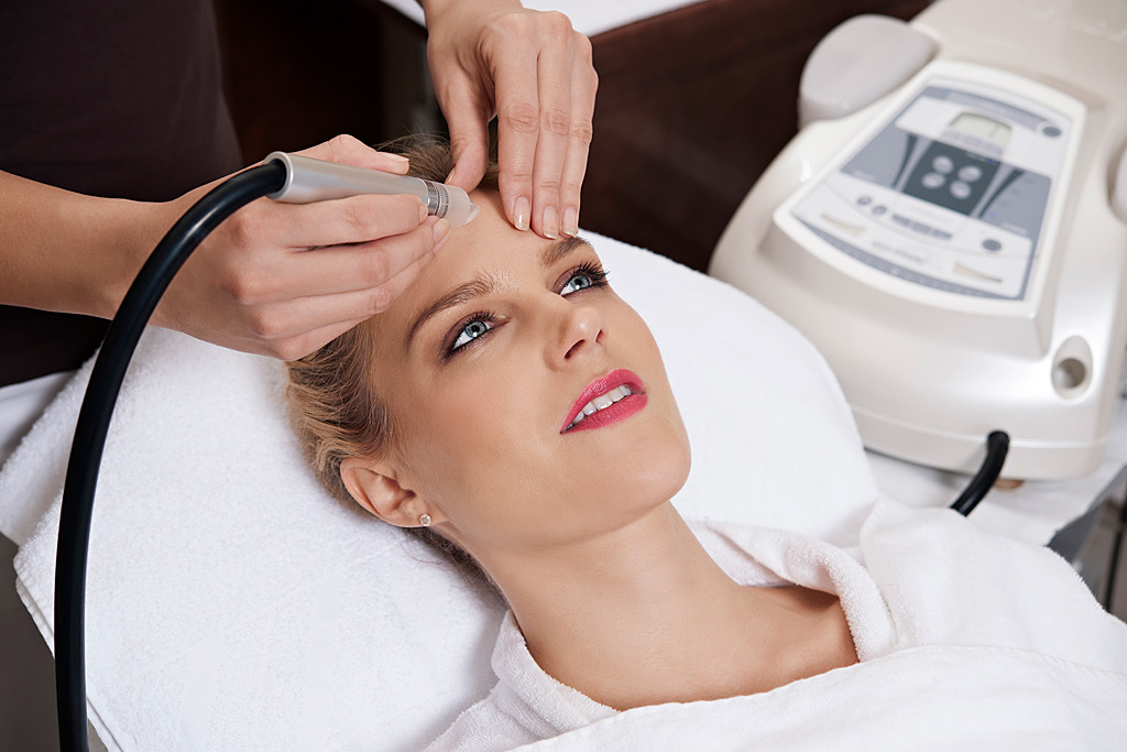 Usposobljena kozmetičarka izvaja pacientki tretma obraza s posebno napravo
