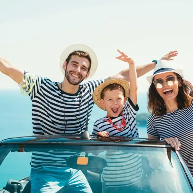 Mlajši moški in ženska z otrokom veselo mahajo iz avtomobila, ki je parkiran ob morju
