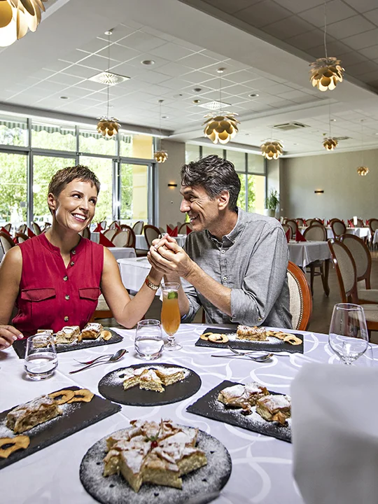 Moški in ženska v srednjih letih sedita za obloženo mizo polno dobrot in se držita za roke