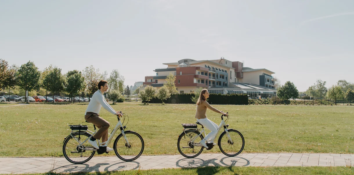 Moški in ženska na kolesu kolesarita po urejeni potki mimo hotela