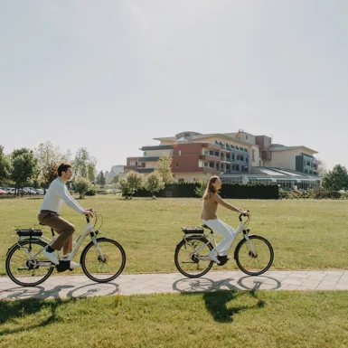 Moški in ženska na kolesu kolesarita po urejeni potki mimo hotela
