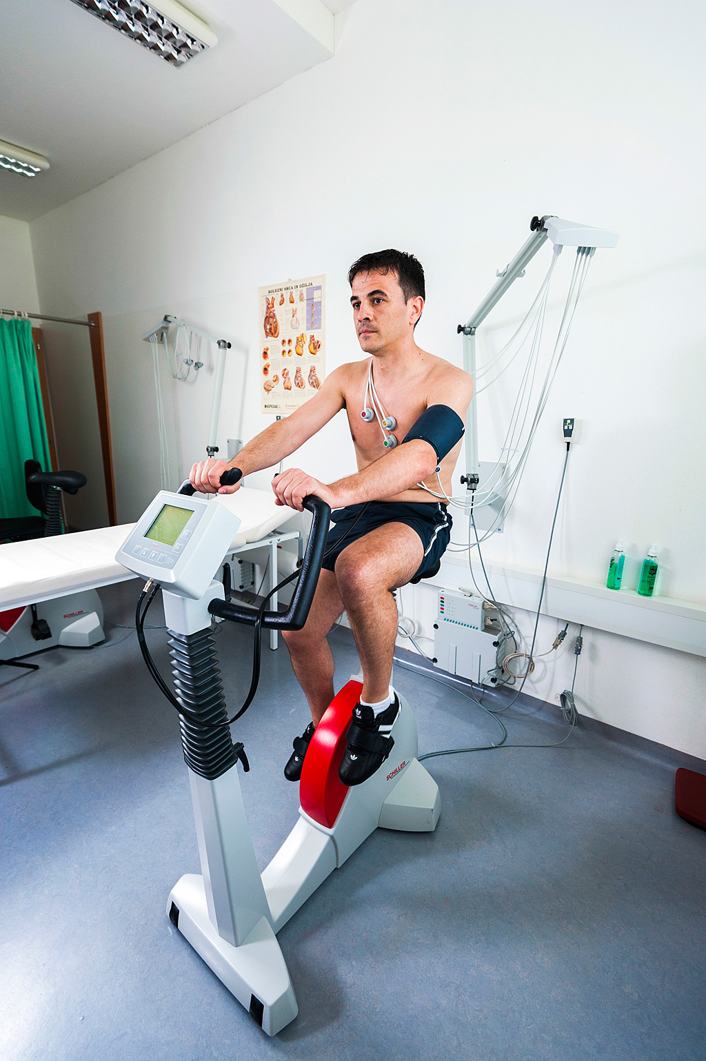 Moški v športnih copatah in hlačkah za oceno tveganja bolezni v ambulanti izvaja test stresa na kolesu