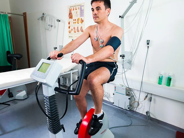 Moški v športnih copatah in hlačkah za oceno tveganja bolezni v ambulanti izvaja test stresa na kolesu