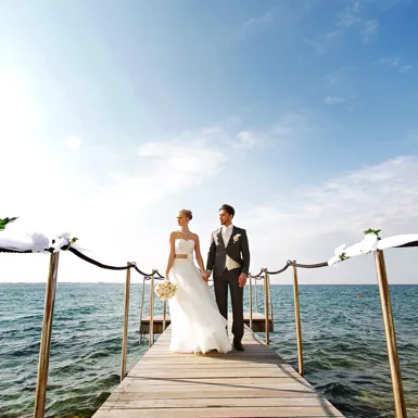 Ženin in nevesta se v poročnih oblekah držita za roke in sprehajata po pomolu ob morju