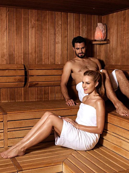 Moški in ženska v belih brisačah uživata in se sproščata v romantični leseni savni