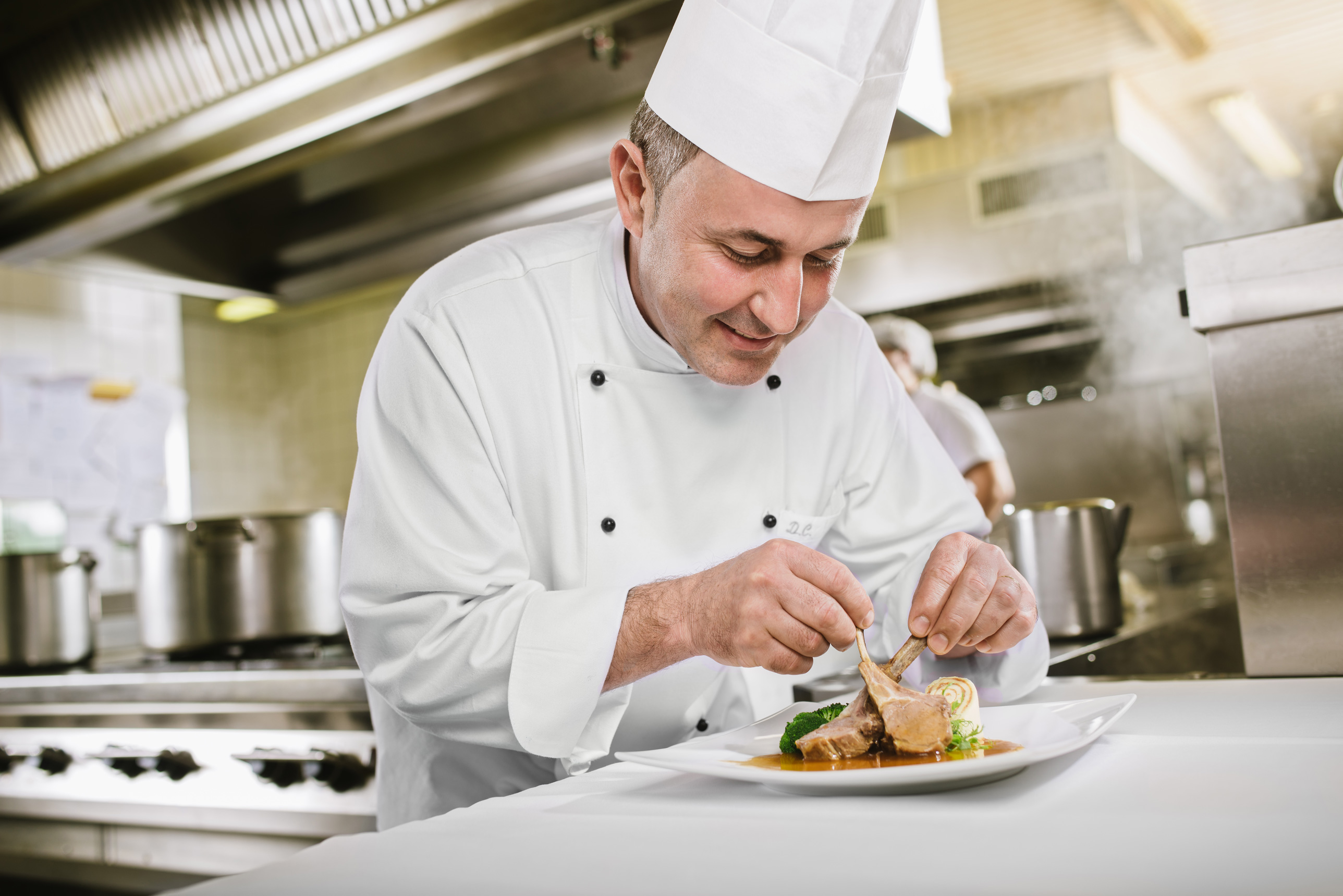 Kuharski mojster Danilo Čurman v kuharskih oblačilih v kuhinji pripravlja jed