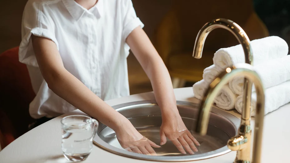 Ženska v beli srajci namaka roke v umivalnik, ki je poln vode