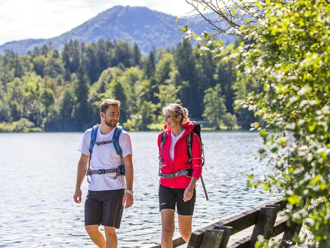 Moški in ženska v športnih oblačilih in s pohodniškim nahrbtnikom pešačita na potki okrog jezera