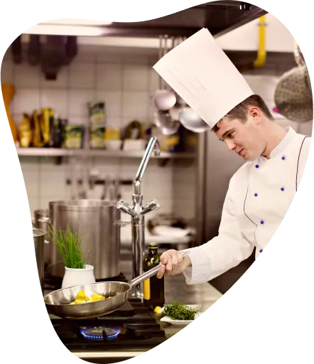 Kuharski mojster Simon Bertoncelj v kuharskih oblačilih v kuhinji pripravlja jed