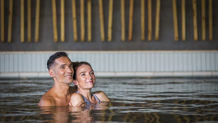 Moški in ženska se v notranjem bazenu objemata in zamišljeno gledata naprej