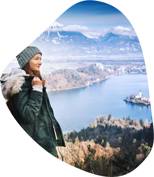 Ženska v zimskih oblačilih stoji na razgledni točki in opazuje otoček na blejskem jezeru